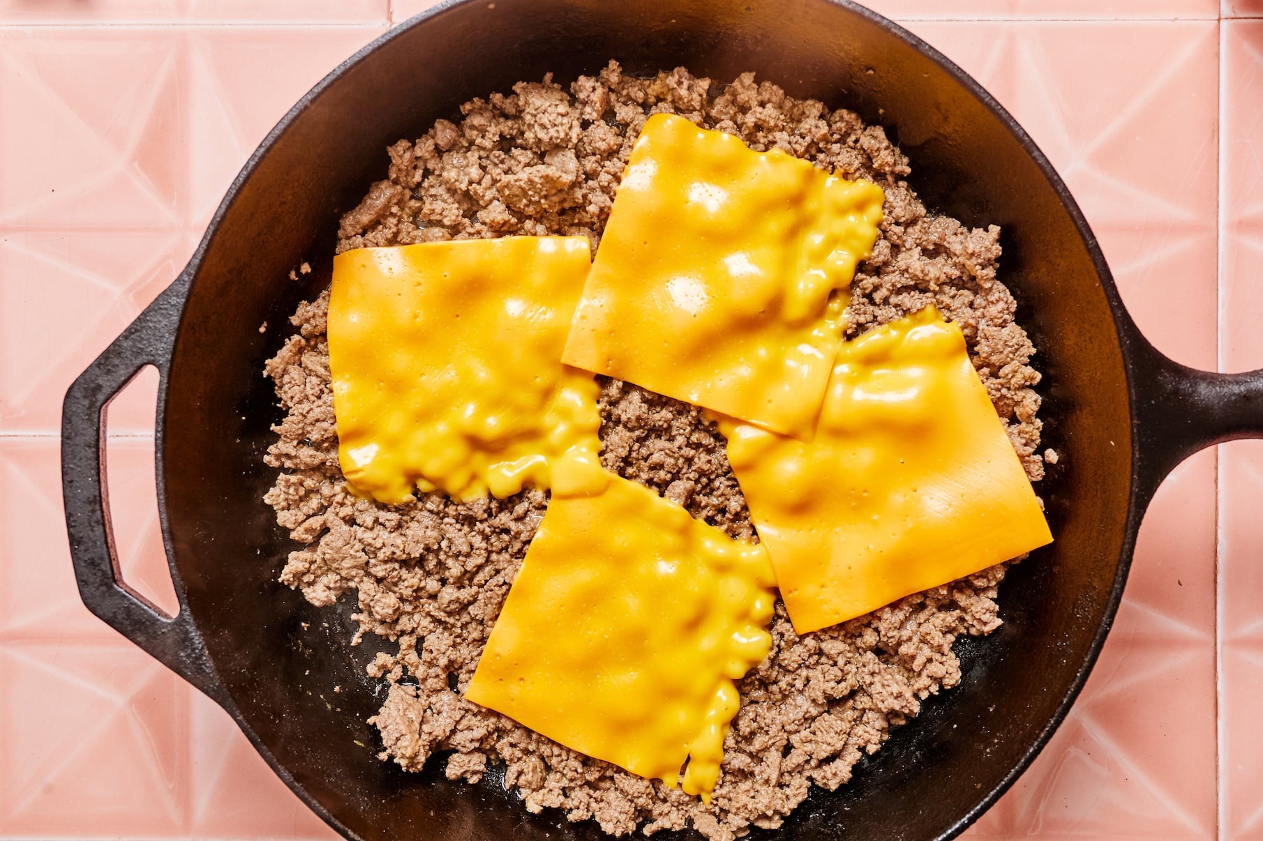 Cooked ground beef topped with melted cheddar cheese in a skillet.