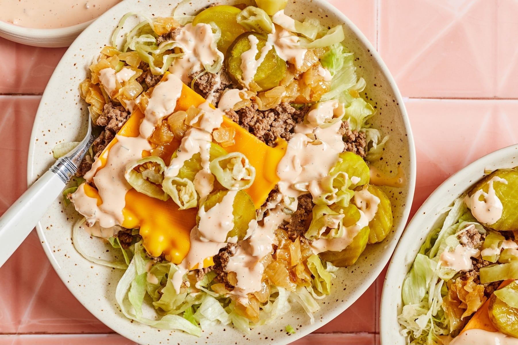 Cheeseburger salad assembled in bowls with iceberg lettuce, cheesy ground beef, caramelized onions, dill pickles, pepperoncini peppers, and animal sauce.