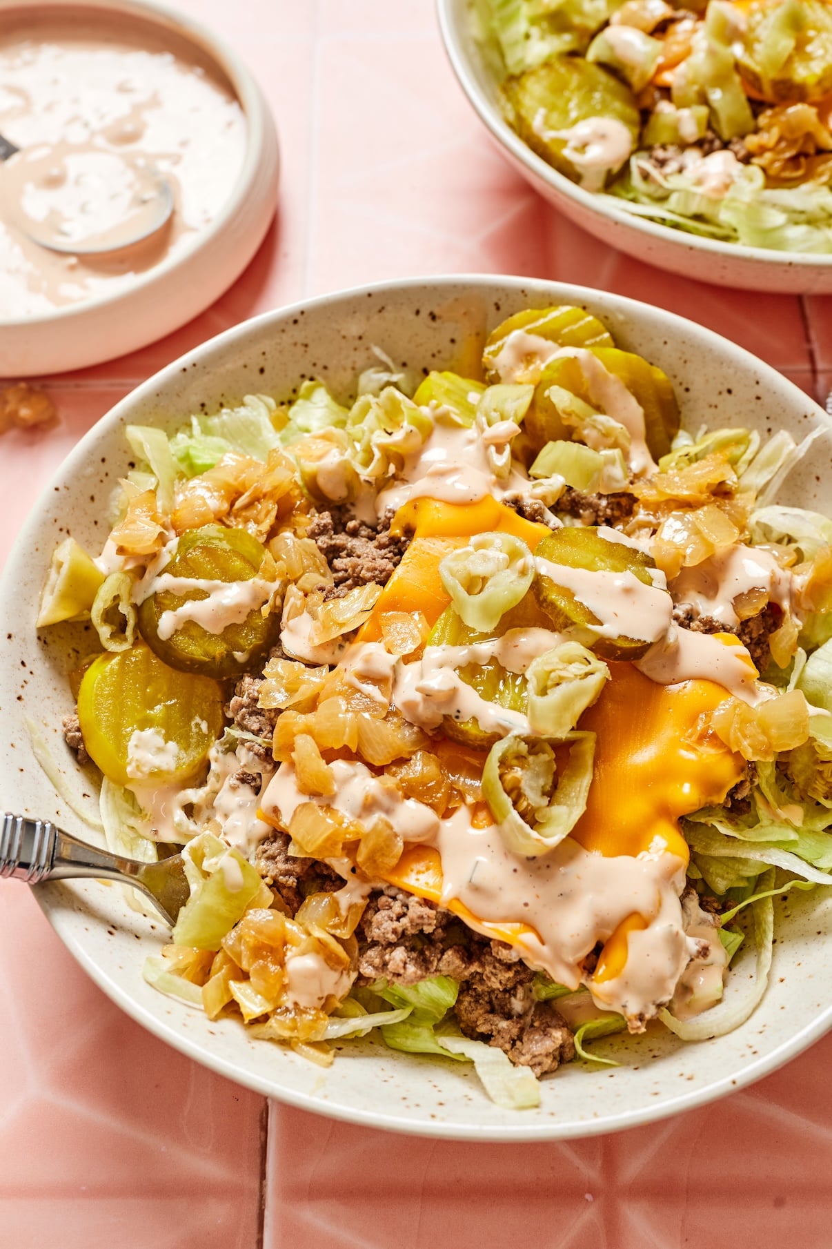 Close-up of cheeseburger salad topped with animal sauce, with a bowl of extra sauce in the background.