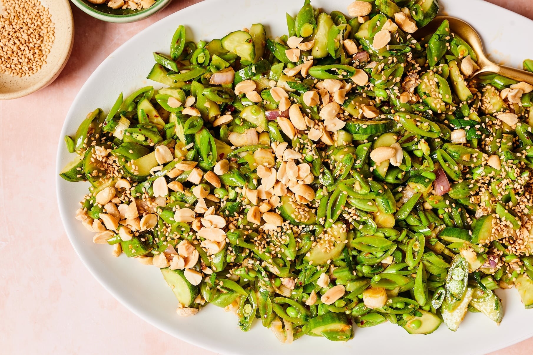 Sugar snap pea salad with cucumbers, cilantro, peanuts, and sesame seeds served on a white platter.