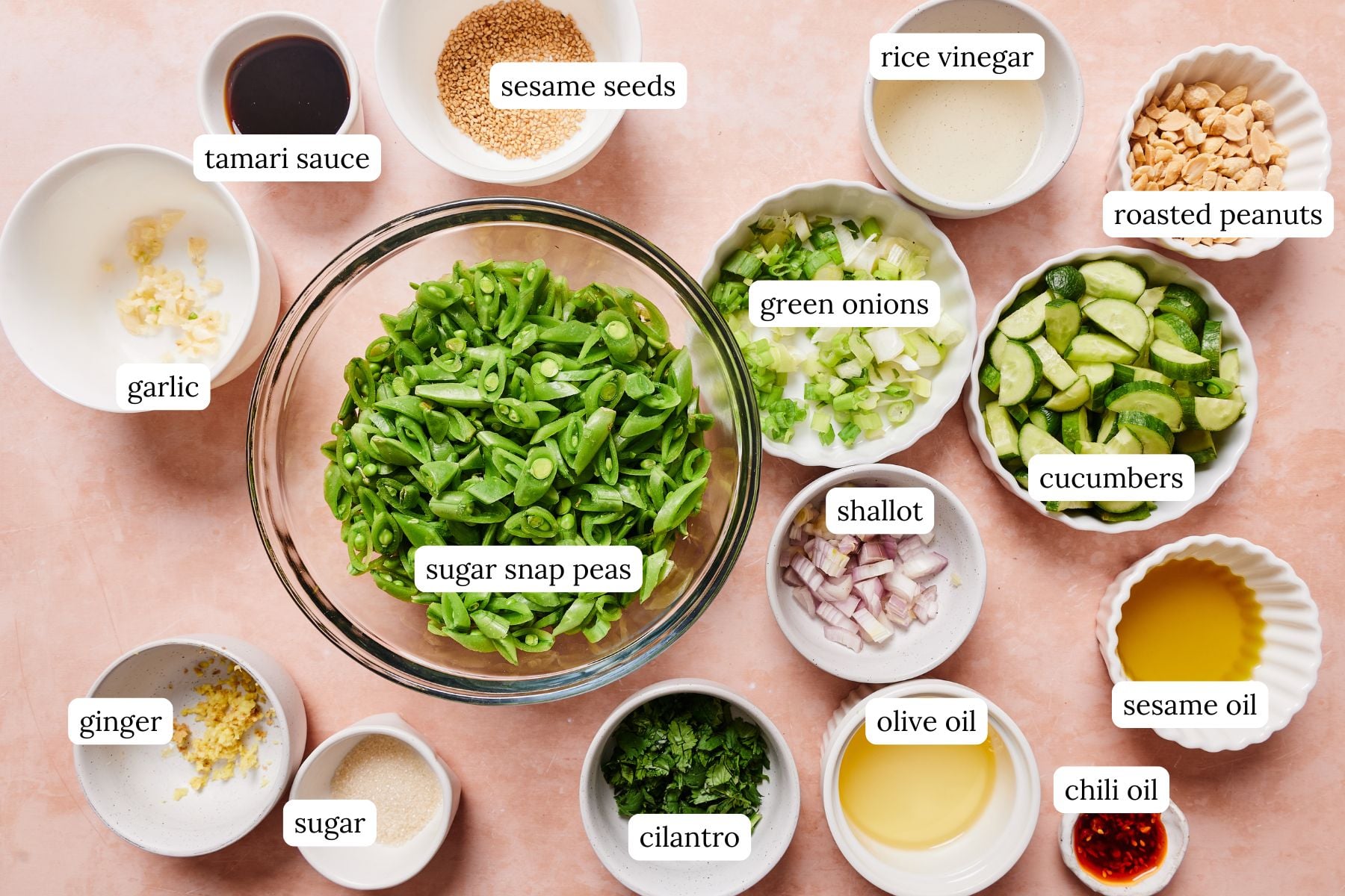 Sugar snap pea salad recipe ingredients laid out and labeled on a light pink countertop.