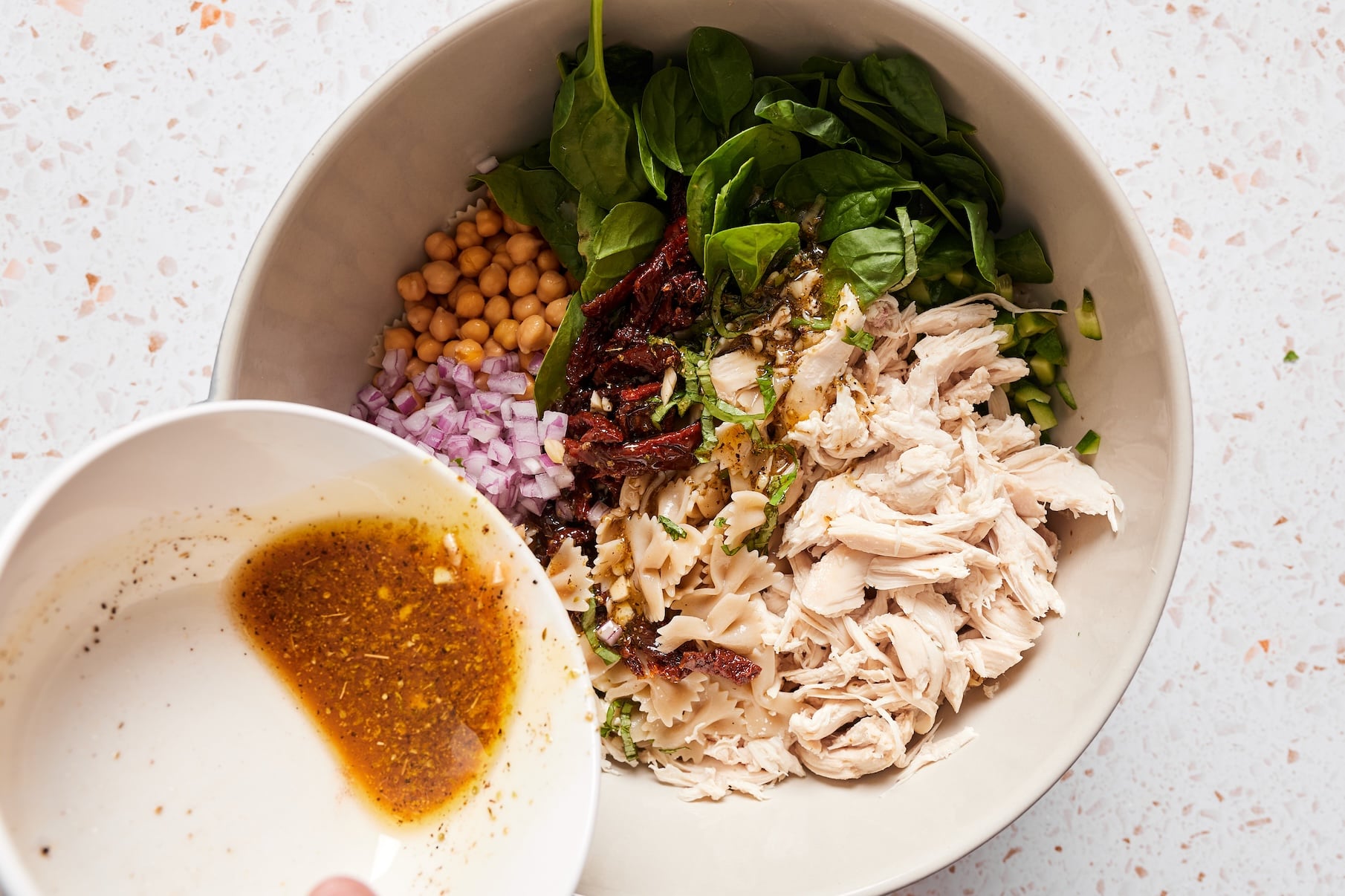 Homemade dressing being poured into a large serving bowl with chickpea pasta salad ingredients.