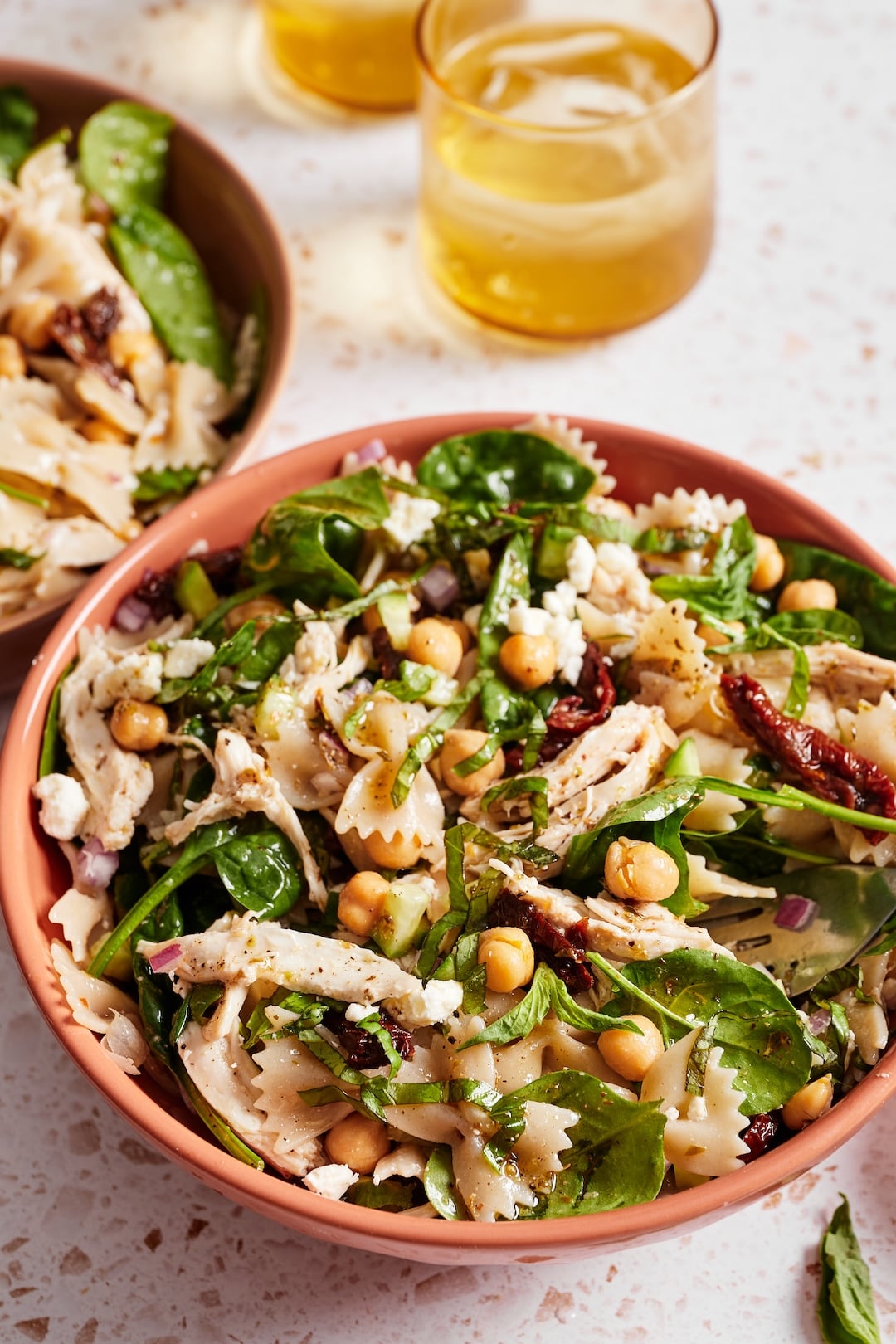 Close-up of a bowl of chickpea pasta salad with shredded rotisserie chicken, feta cheese, fresh vegetables, and homemade vinaigrette.