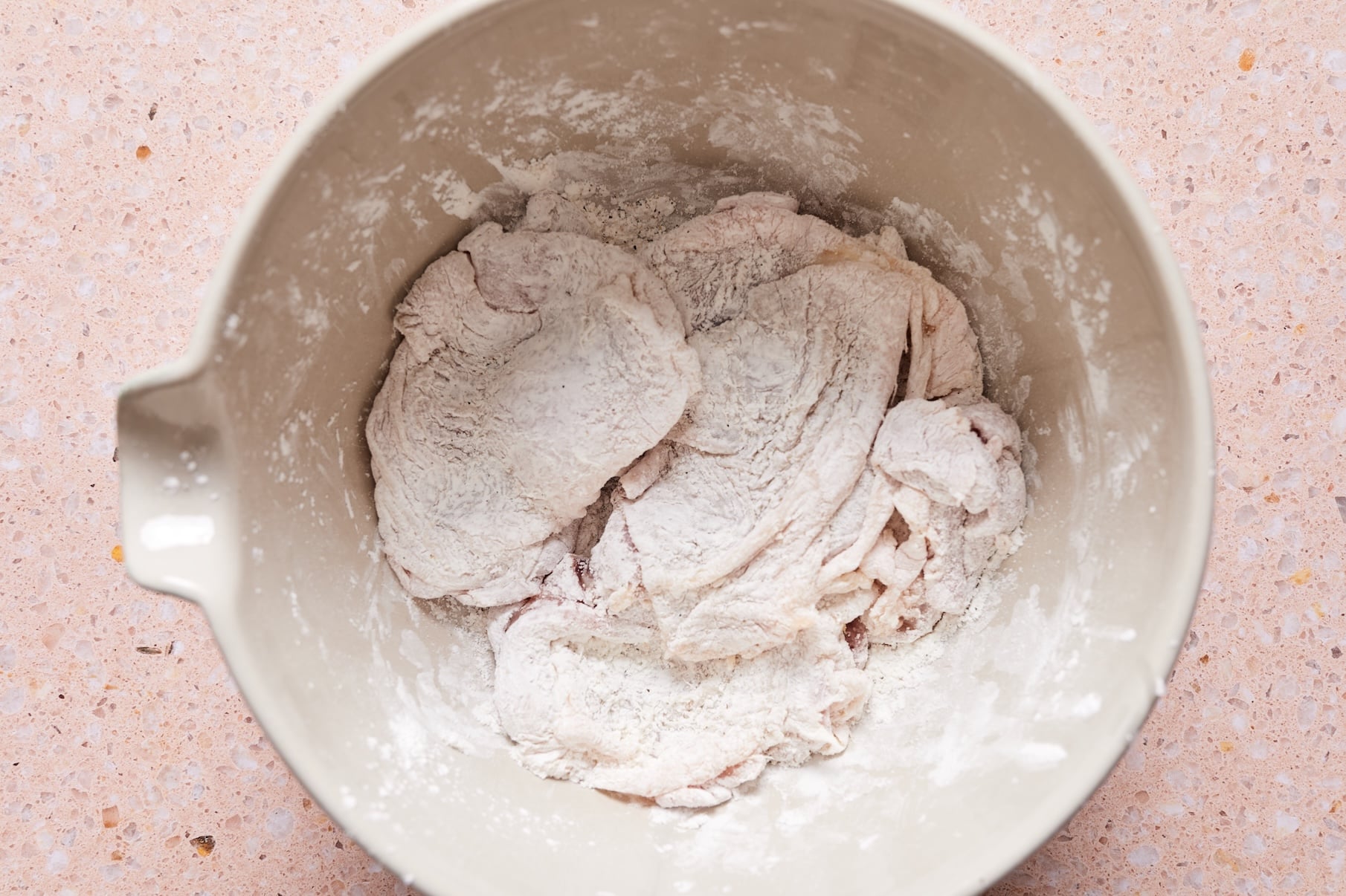 Chicken thighs in a mixing bowl coated with cornstarch.