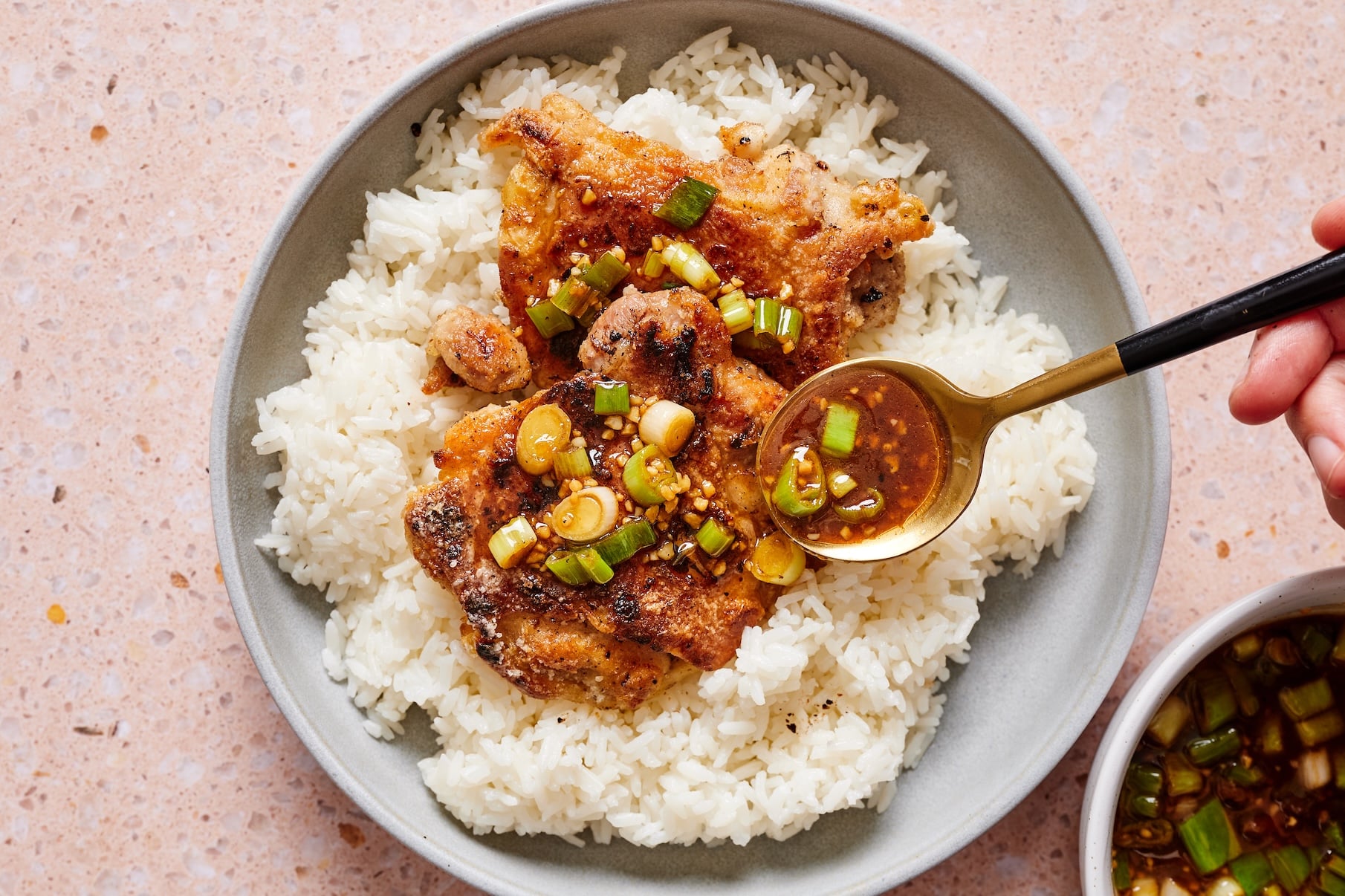 Gray bowl filled with rice and crispy scallion chicken as savory scallion sauce is drizzled over the top.