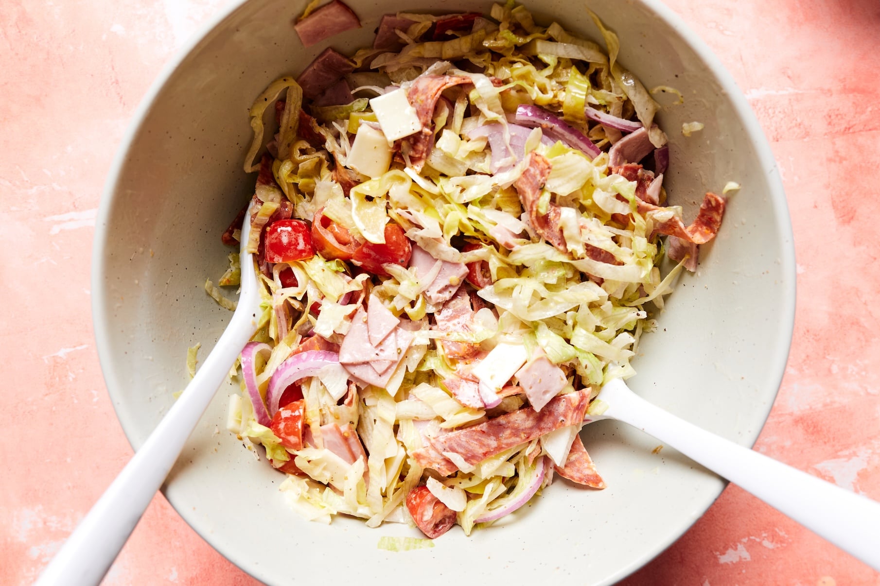 Creamy Italian dressing poured over a sub in a tub salad before tossing to coat the lettuce, deli meats, cheese, and vegetables.