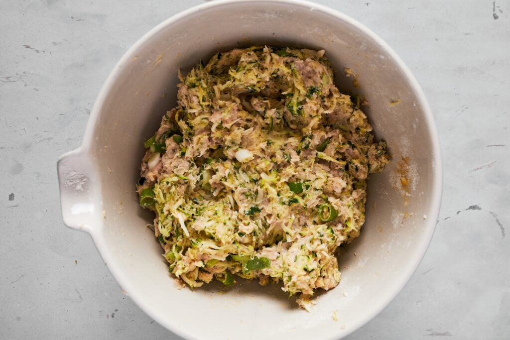 Squeezed zucchini, ground chicken, egg, green onions, garlic, mozzarella, flour, and ground black pepper in a large bowl.