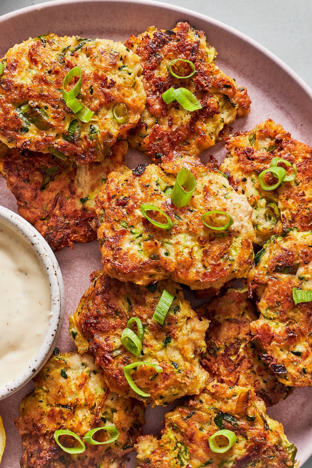 A plate of gluten-free zucchini fritters garnished with green onions and a side of garlic aioli.