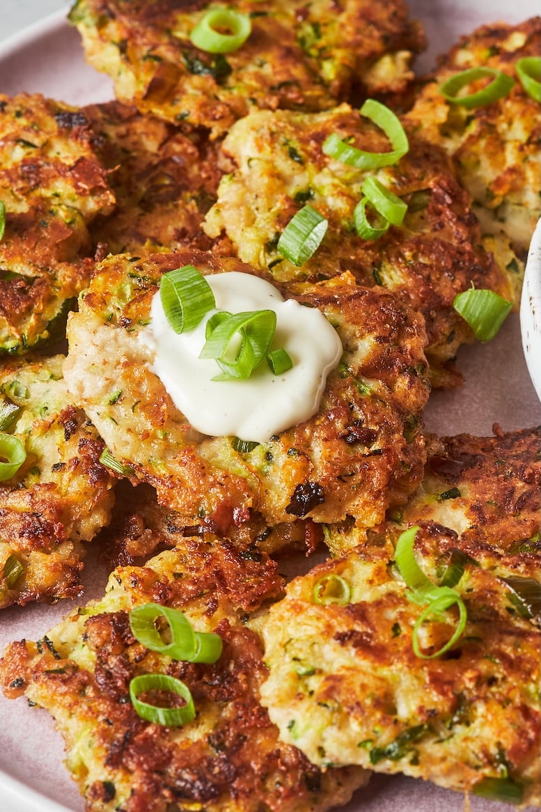 Zucchini fritters topped with green onions served on a pink plate with creamy garlic aioli.