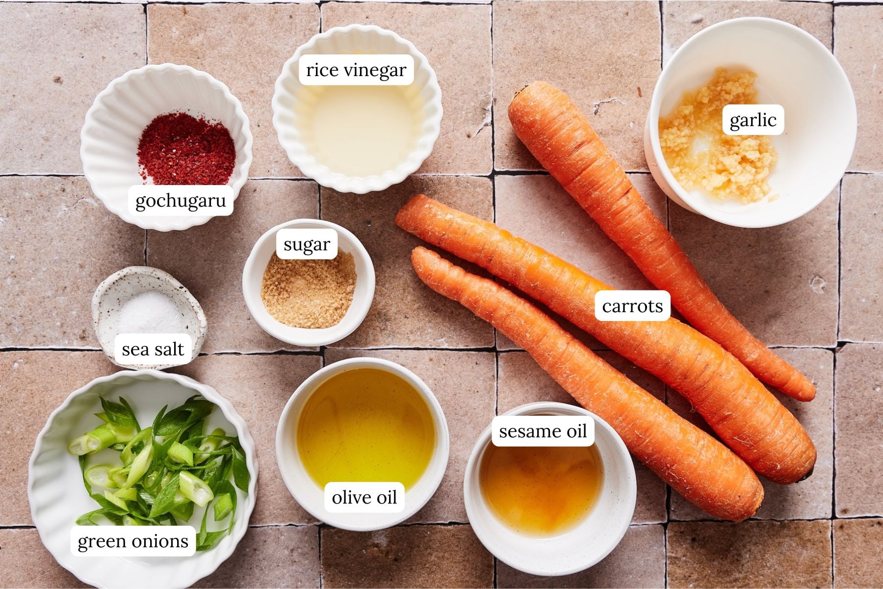 Korean carrot salad recipe ingredients laid out and labeled on a tiled countertop.