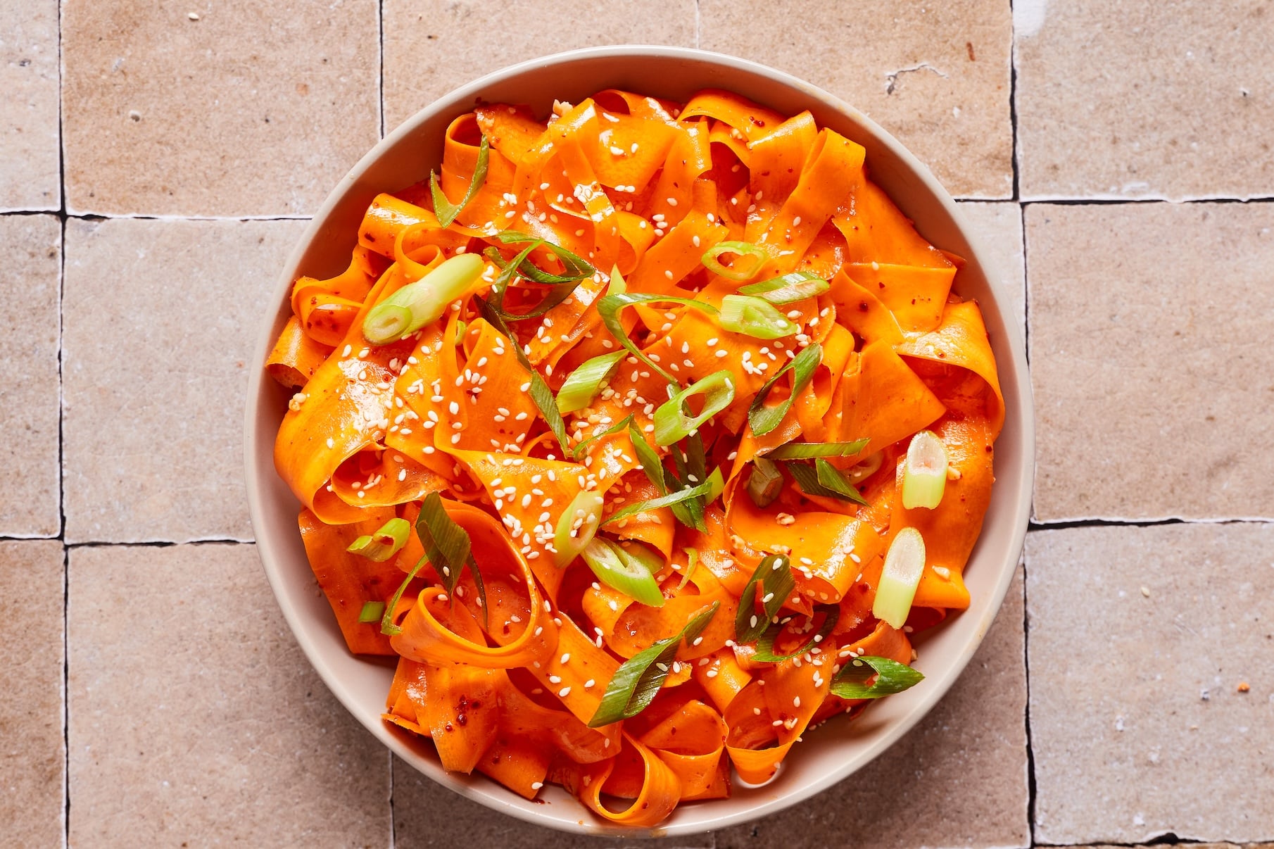 Korean carrot salad in a bowl garnished with green onions and toasted sesame seeds.