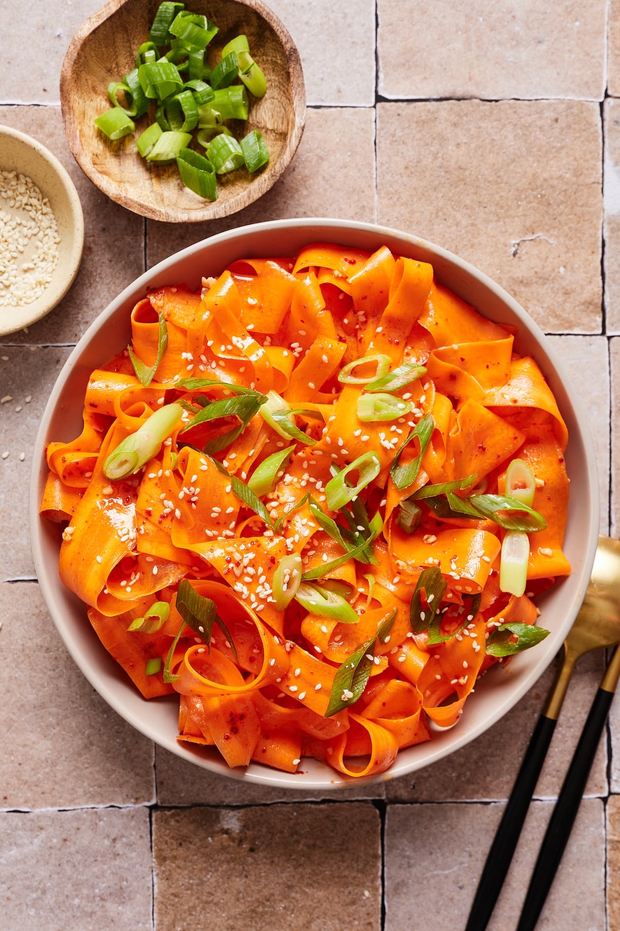 Korean carrot salad in a small bowl garnished with green onions and toasted sesame seeds.