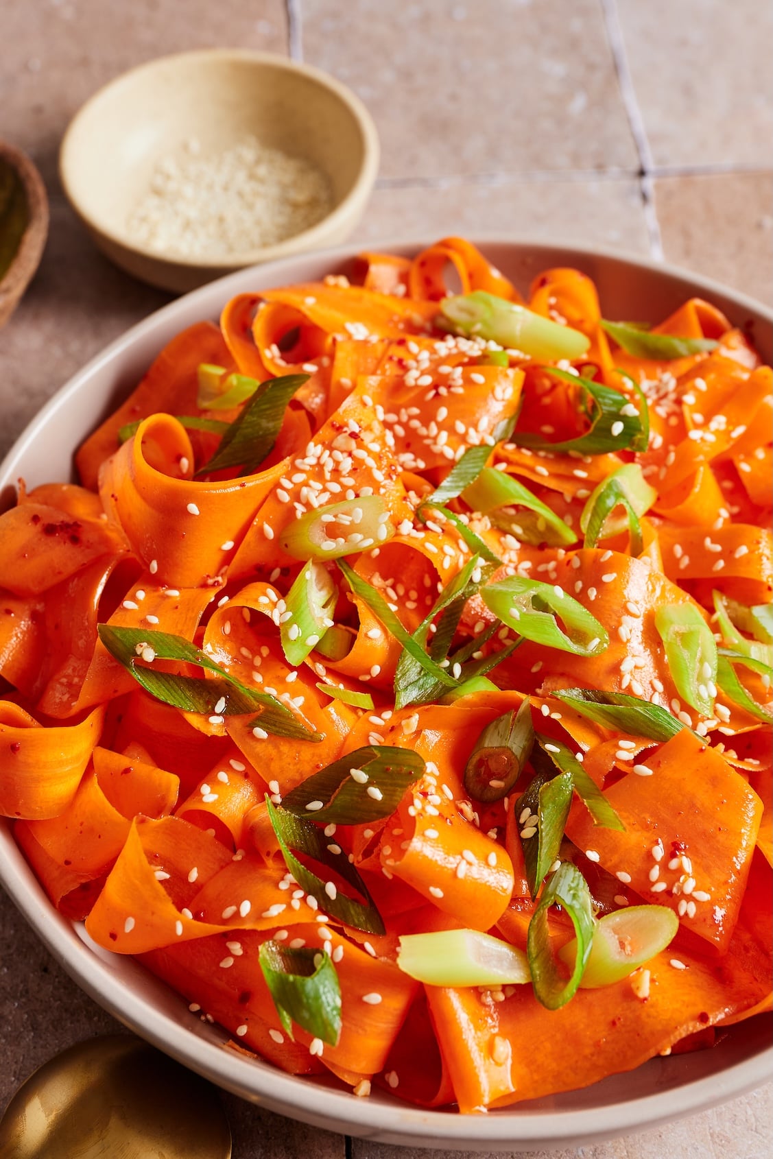Close-up of Korean carrot salad in a bowl garnished with green onions and toasted sesame seeds.