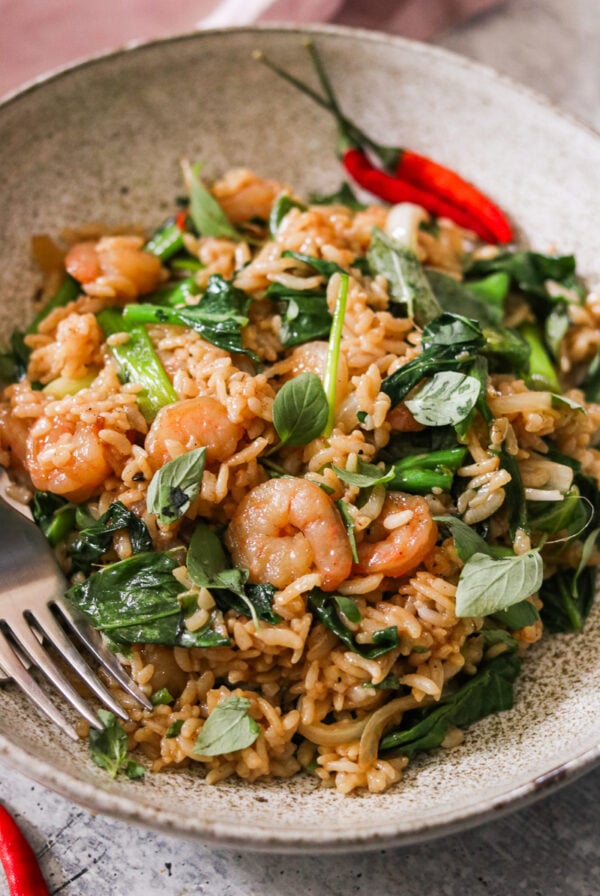 an up close shot of drunken fried rice topped with cooked shrimp and fresh Thai basil.