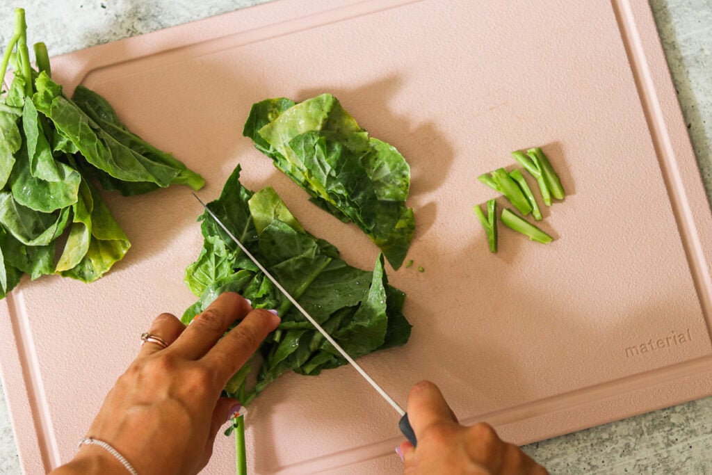 a hand cutting greens on a pink cutting board.