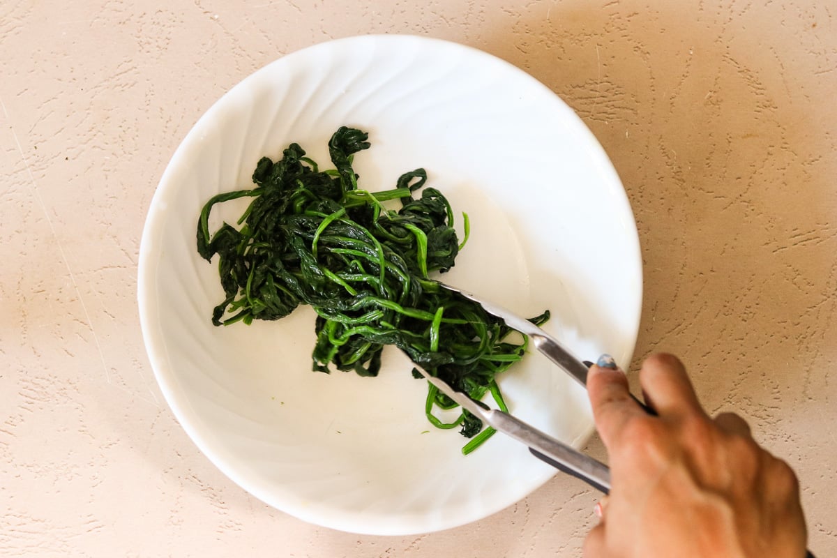 Blanched spinach tossed with sesame oil and sea salt in a bowl.