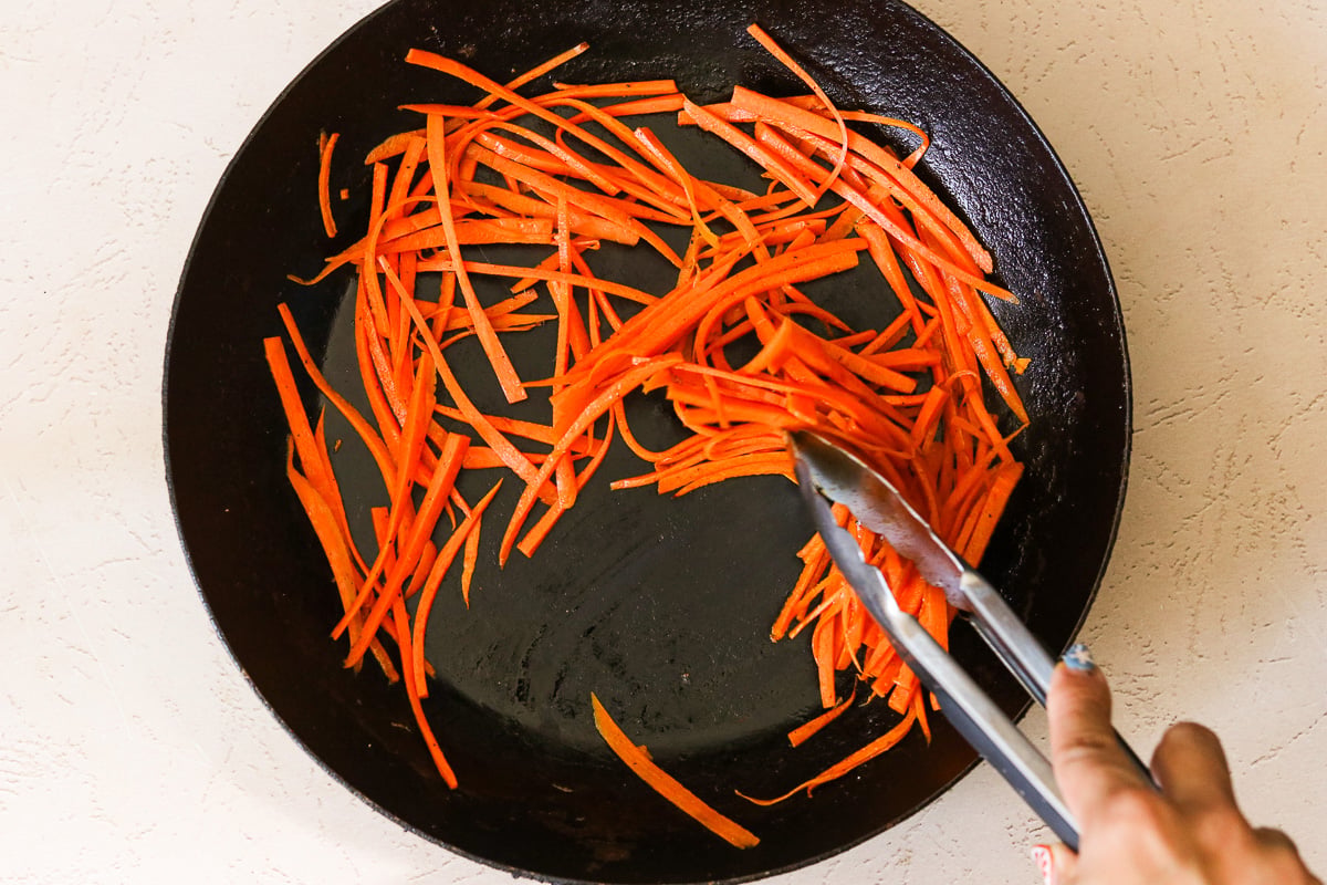 Sliced carrots sautéing with sesame oil and sea salt in a skillet.