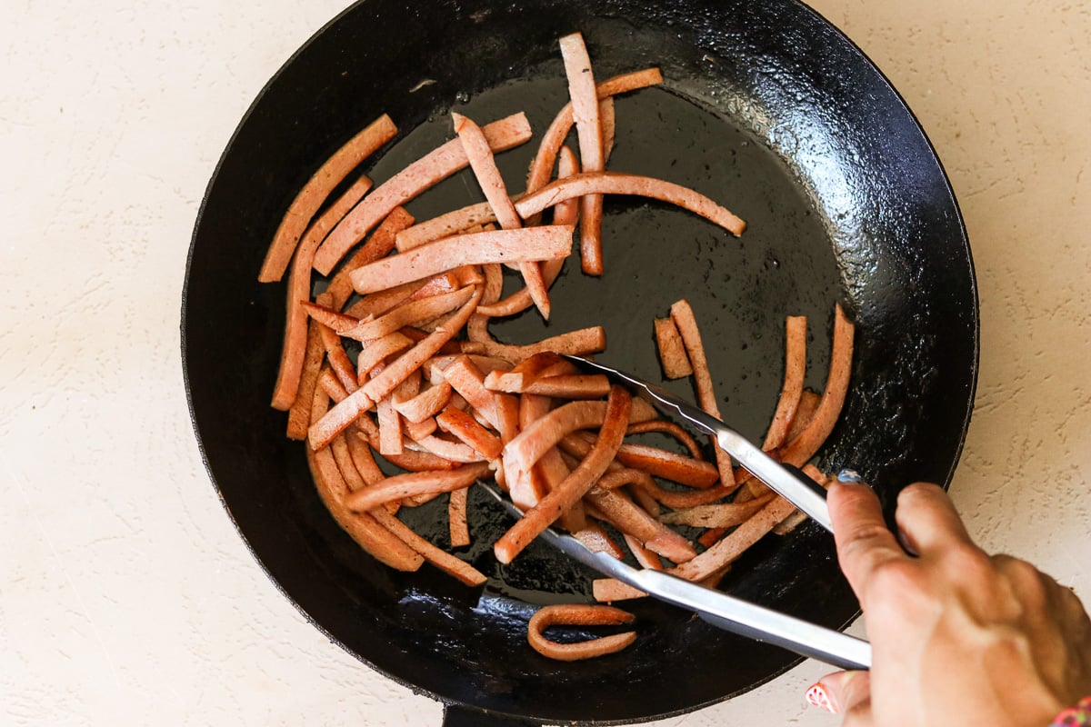 Sliced Spam cooking in a skillet until lightly charred on the outside.