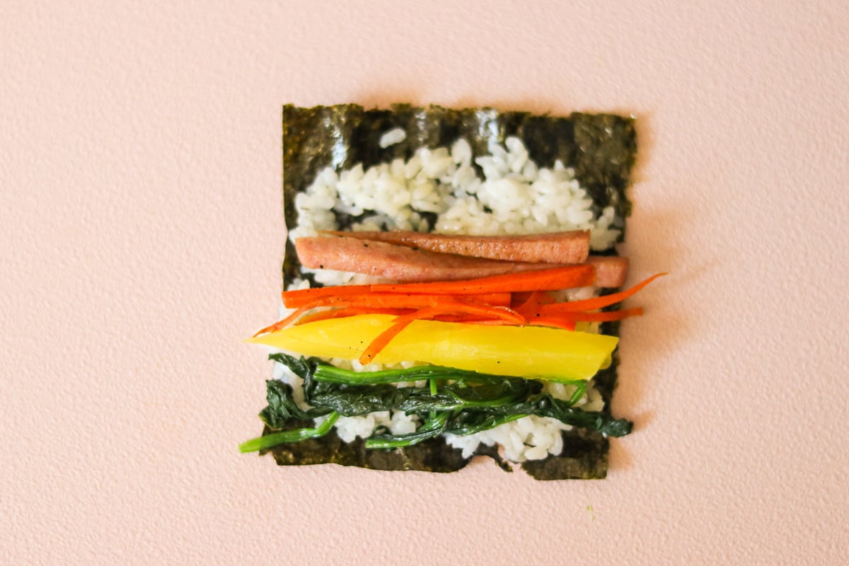 Rice spread evenly over a quartered seaweed sheet, leaving space along the top edge.