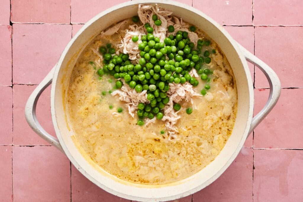 Incorporating the peas and chicken into the chicken pot pie soup ingredients in a Dutch oven.