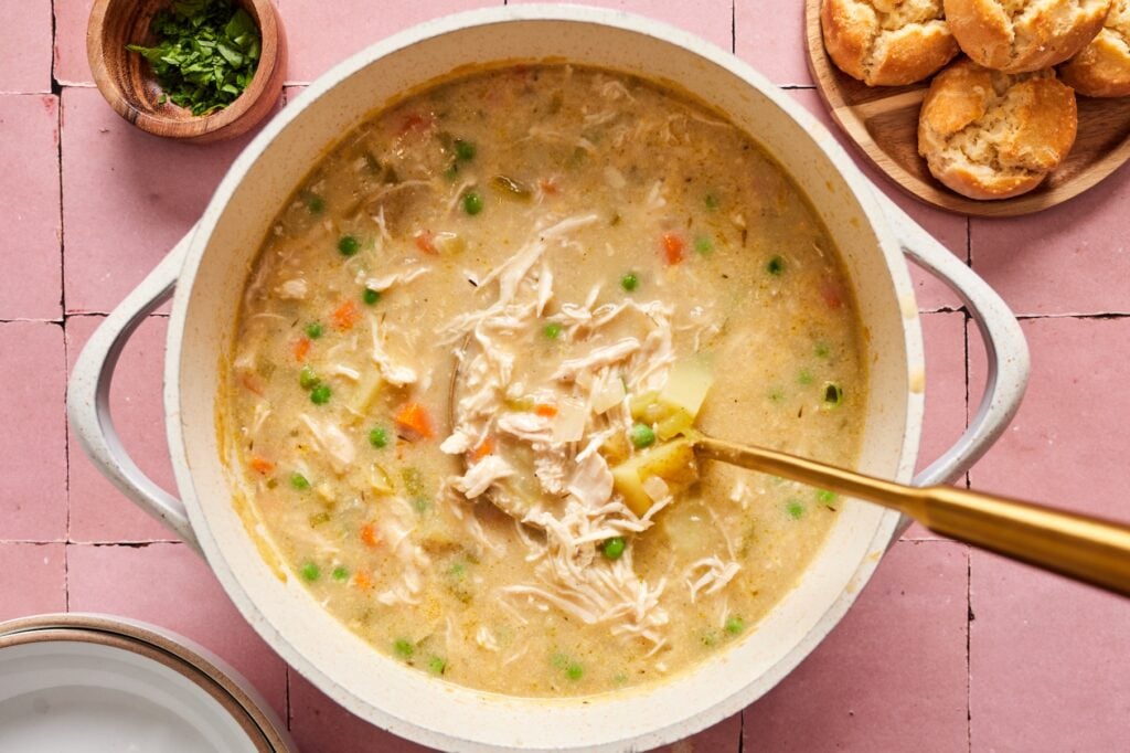 A gold spoon stirring a finished chicken pot pie soup recipe in a Dutch oven.