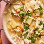 A bowl of chicken pot pie soup in a bowl showing the peas, chicken, carrots, and potatoes.