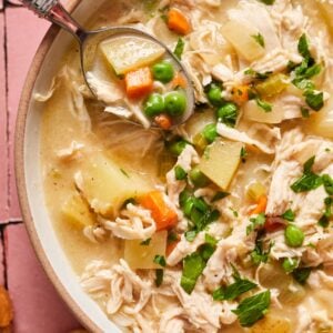 A bowl of chicken pot pie soup in a bowl showing the peas, chicken, carrots, and potatoes.