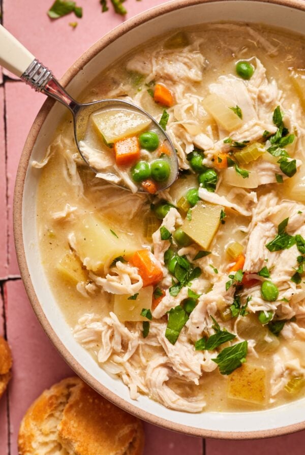 A bowl of chicken pot pie soup in a bowl showing the peas, chicken, carrots, and potatoes.