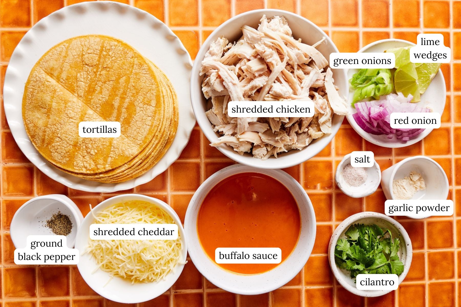 Ingredients for crispy buffalo chicken tacos laid out and labeled on a tiled countertop.