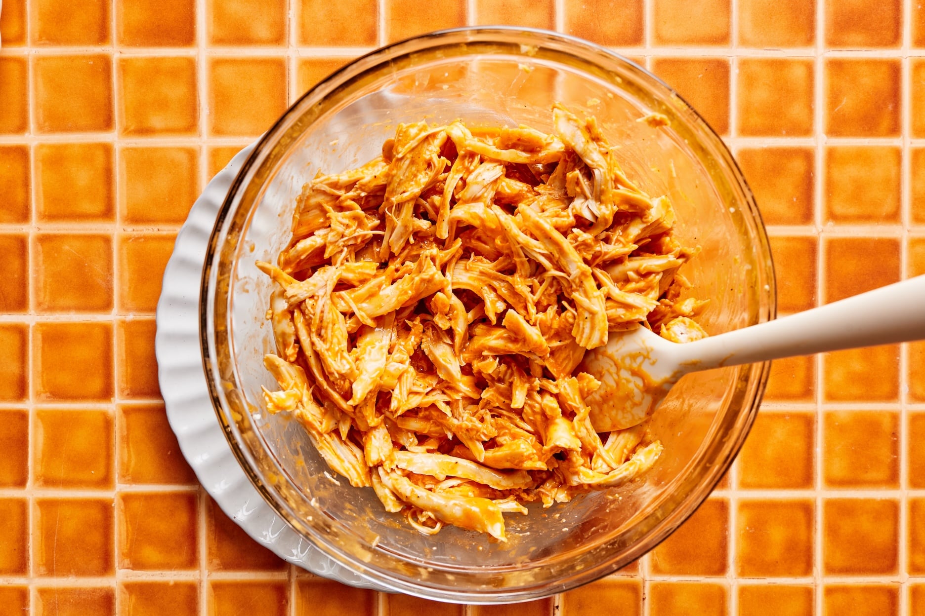 A large bowl with shredded chicken, coated in buffalo sauce, garlic powder, sea salt, and black pepper.