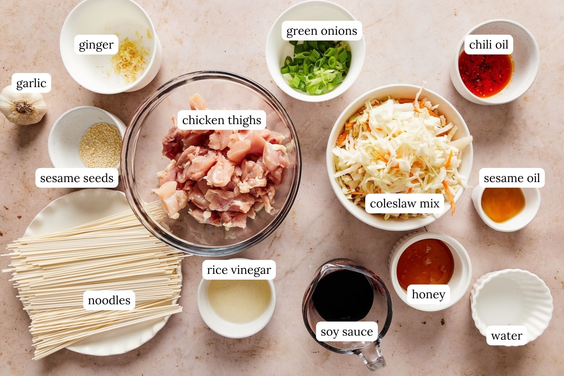 Honey garlic chicken noodle recipe ingredients arranged and labeled in bowls on a countertop.