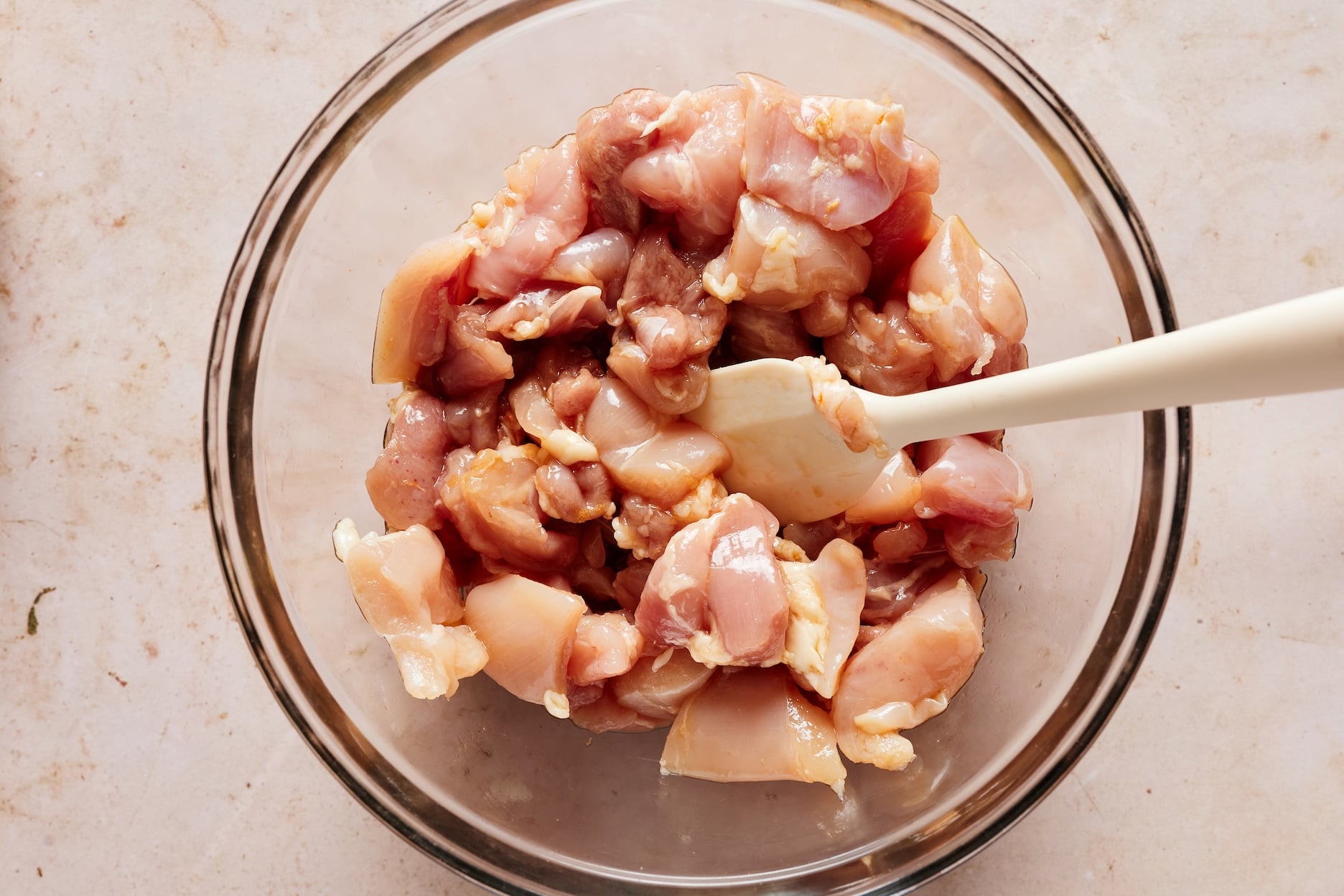Raw chicken tossed with the honey garlic sauce in a glass bowl.