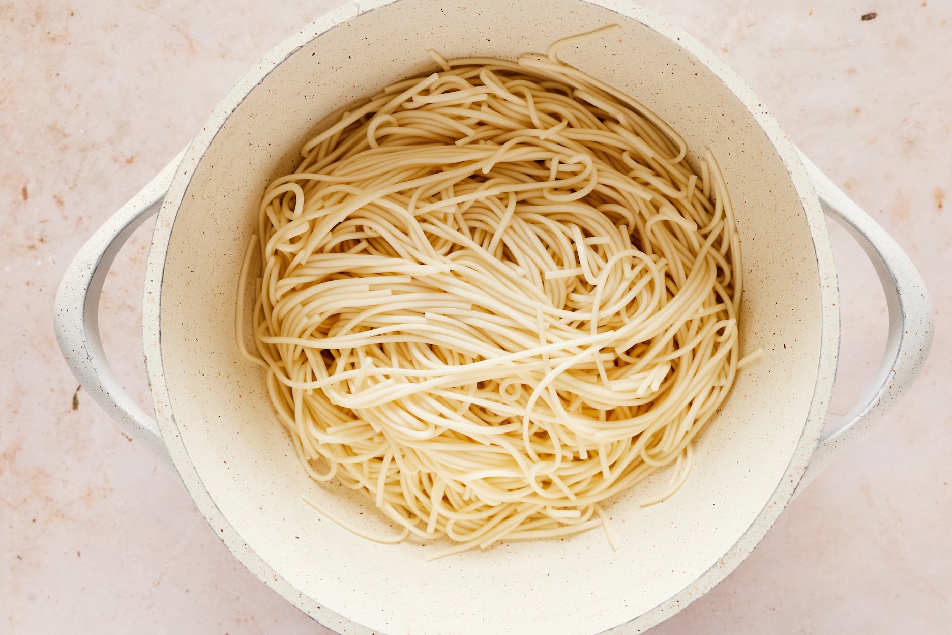 Soaked and drained rice noodles in a white colander.
