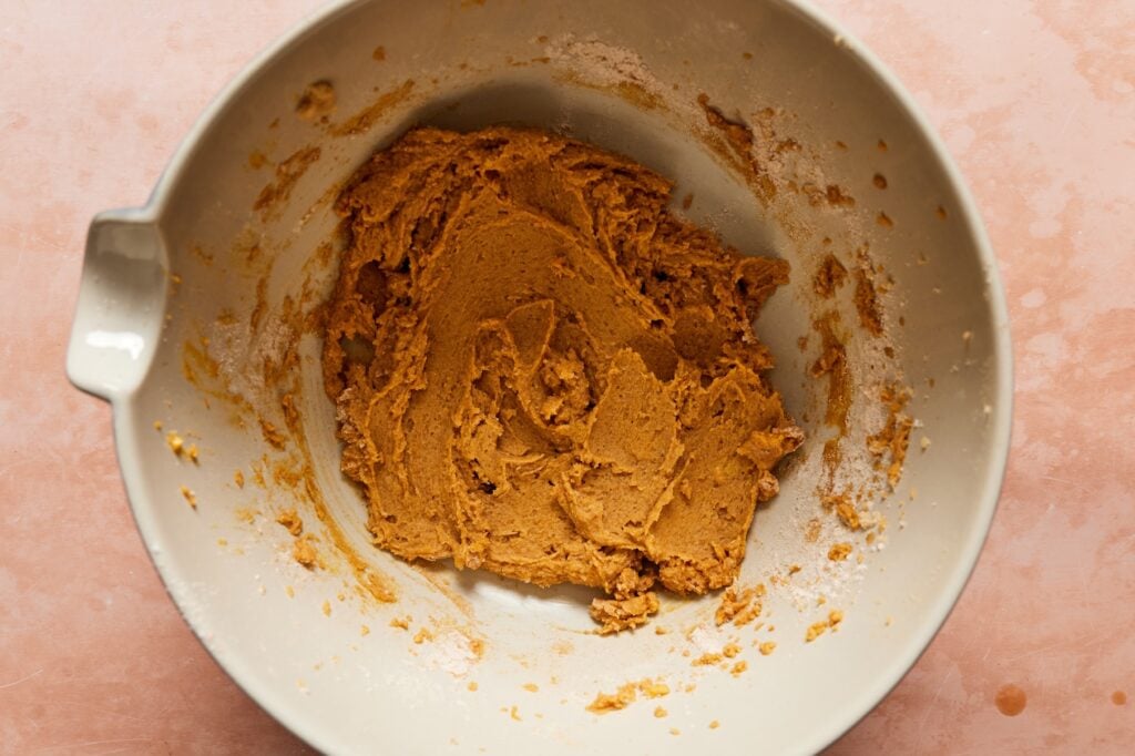 A bowl with creamed butter, sugar, and pumpkin puree in a mixing bowl.