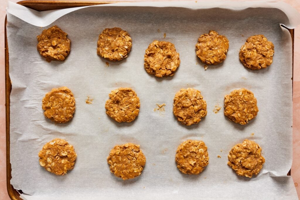 Flattened pumpkin oatmeal cookies on a lined baking sheet before baking.