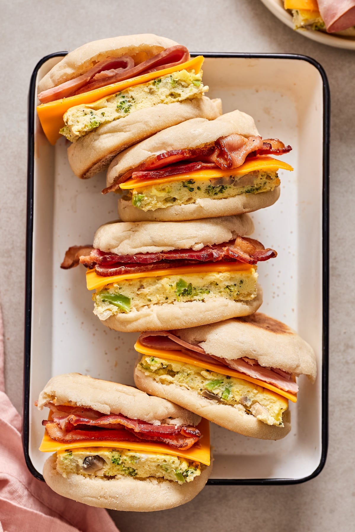 Five breakfast sandwiches on their sides showing the muffin, egg, cheese, meat, muffin assembly.