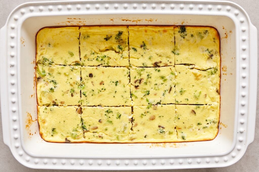 Baked eggs with broccoli, mushrooms, and onion cut into 12 squares in a white 9×13 baking dish