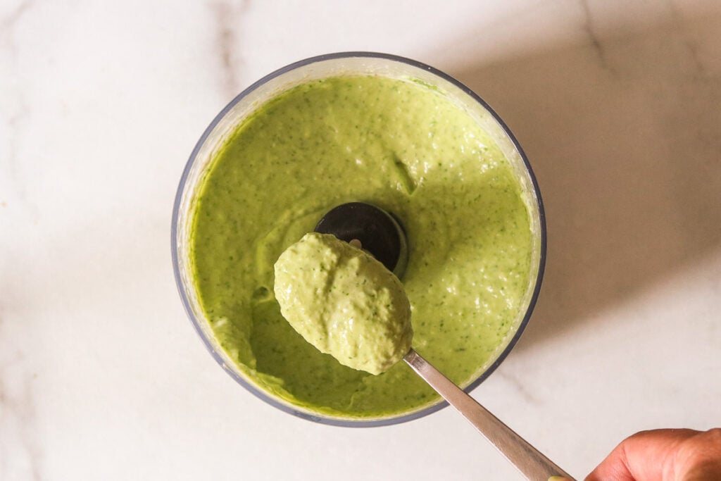a spoon holding a scoop of blended sauce atop a food processor.
