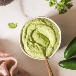 Avocado cilantro sauce in a white bowl with a spoon resting on the side.
