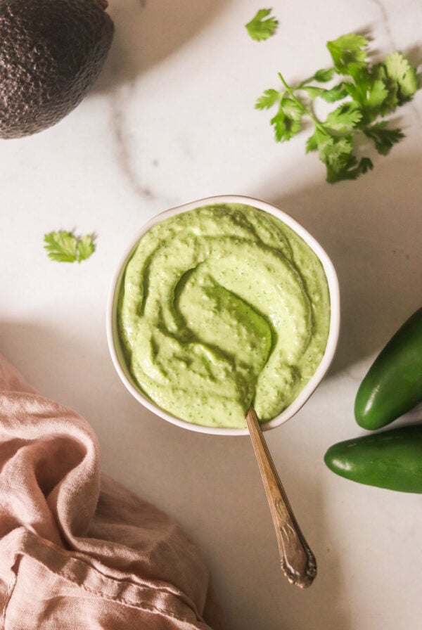 Avocado cilantro sauce in a white bowl with a spoon resting on the side.