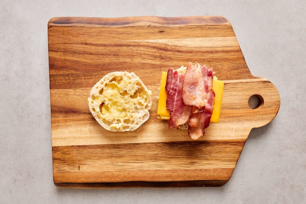 Assembling the freezer breakfast sandwiches from the bottom to the top: muffin, egg, cheese, bacon, muffin.