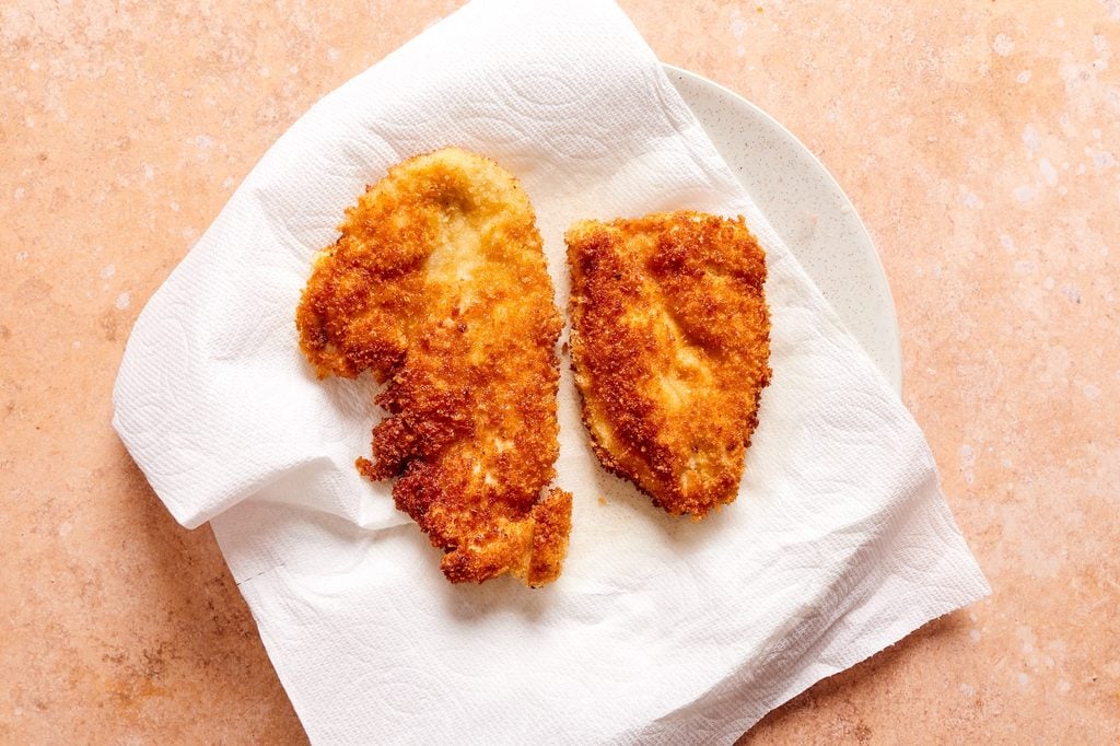 two fried cutlets resting on a plate lined with paper towels.