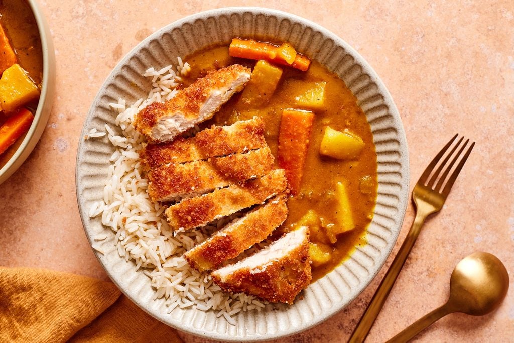 a bowl filled with short grain rice, curry with potatoes, onions, and carrots, and a fried chicken cutlet on top.