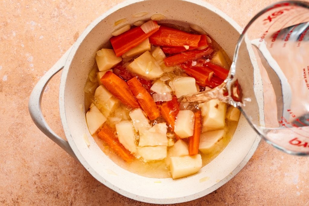 Pouring water over potatoes, carrots, and onion in a soup pot