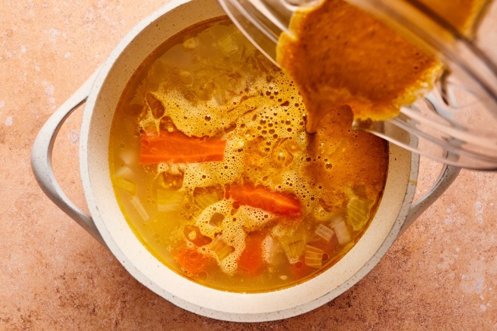 Adding the blended curry to the pot of veggies and water.