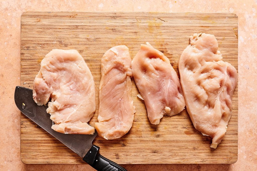Slicing chicken with a large knife on a cutting board to make thin cutlets