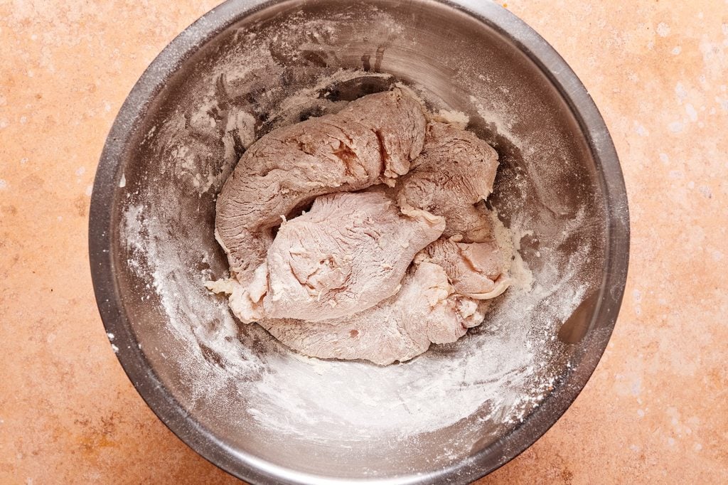 chicken cutlets in a bowl coated with flour.