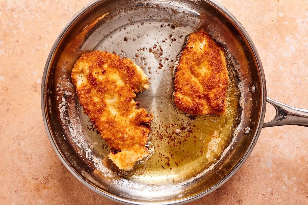 frying the chicken cutlets in oil in a silver pan.