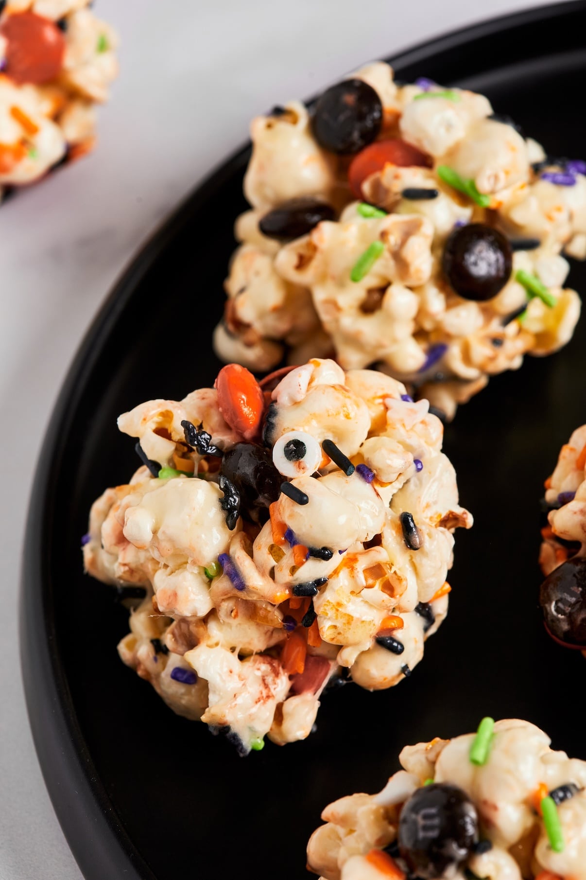 A close up of one popcorn ball rolled in Halloween sprinkles with candy eyeballs pressed on top