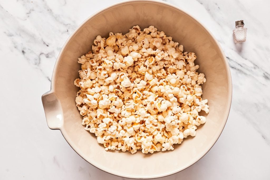 Popped popcorn in a large mixing bowl being sprinkled with sea salt